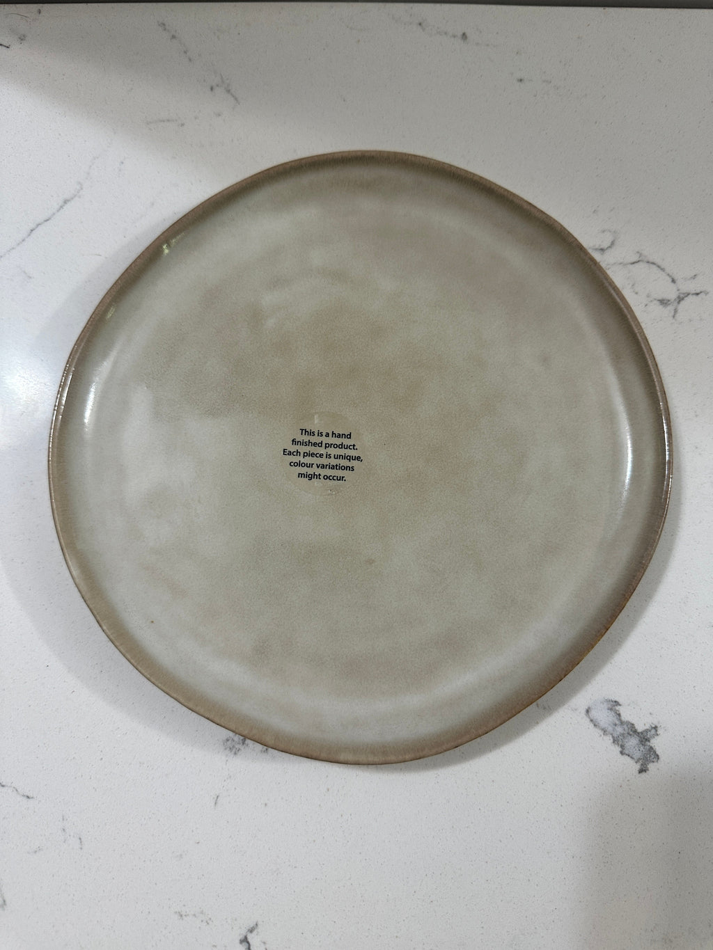 The Collected Chapter AmorArc stoneware dinner plate with a beige reactive glaze and a brown rim on a white surface.