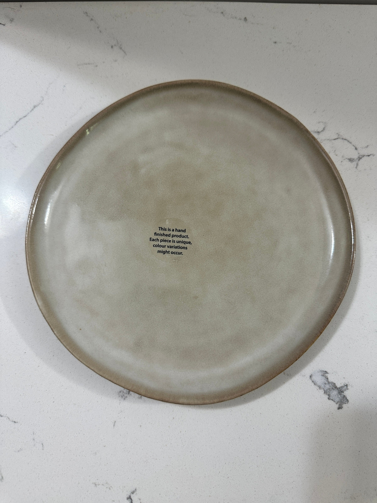 The Collected Chapter AmorArc stoneware dinner plate with a beige reactive glaze and a brown rim on a white surface.