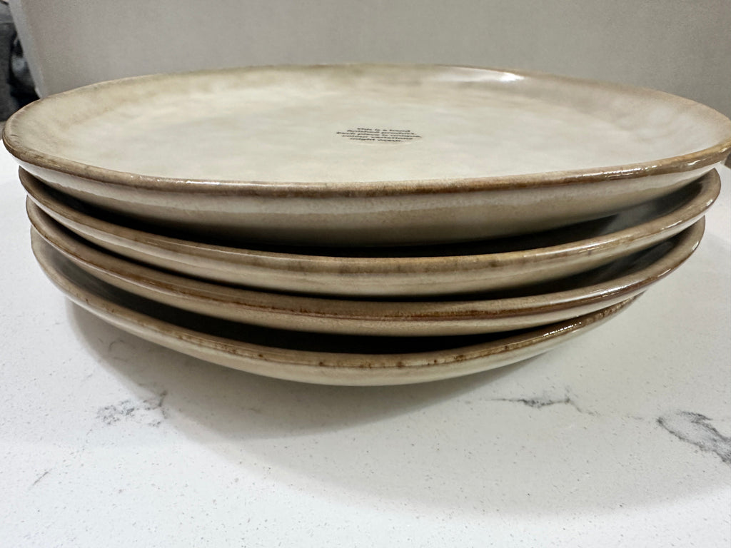 The Collected Chapter AmorArc handcrafted stoneware dinner plates in beige with a rustic reactive glaze and brown rims.