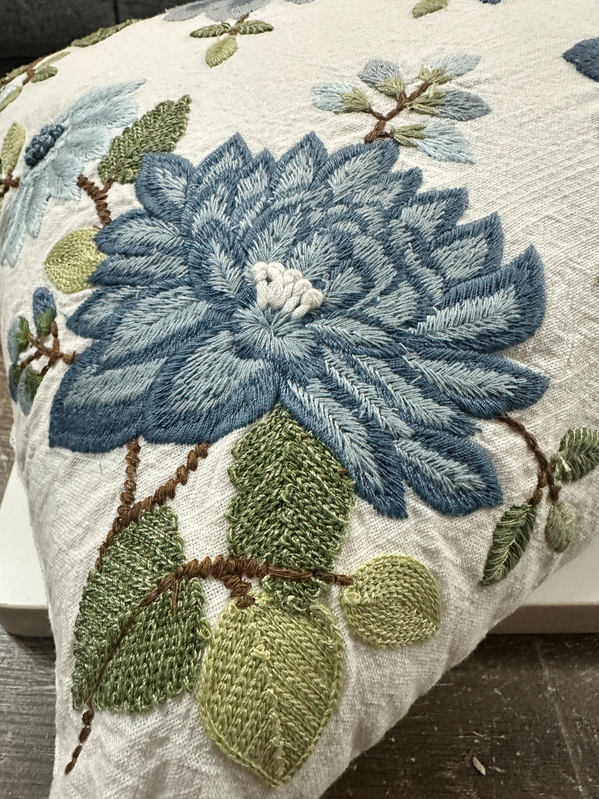 The Collected Chapter lumbar pillow with dense blue floral embroidery and sage green leaves on textured cream fabric.