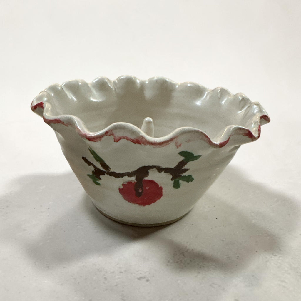 The Collected Chapter handmade ceramic apple baker with a creamy white glaze, ruffled edge, and painted apple motif.