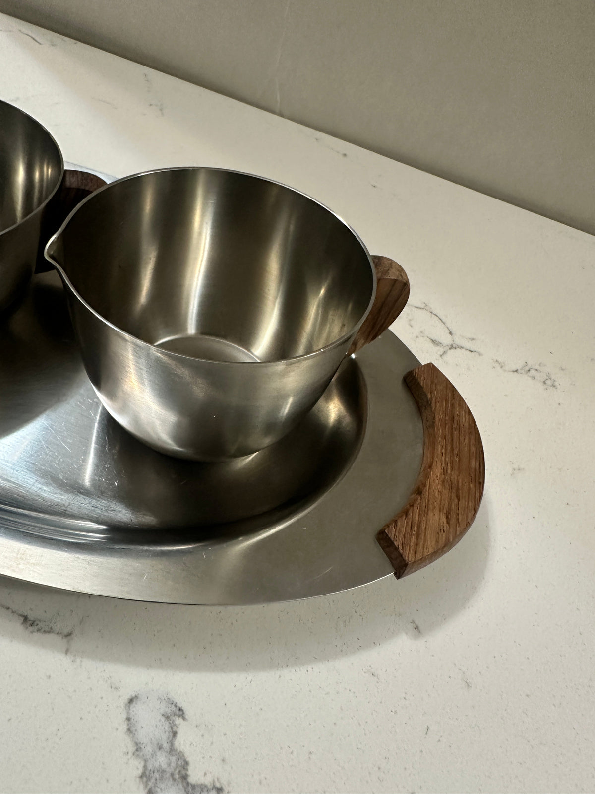 The Collected Chapter vintage Danish Modern stainless steel creamer and sugar set with wood handles on an oval tray.