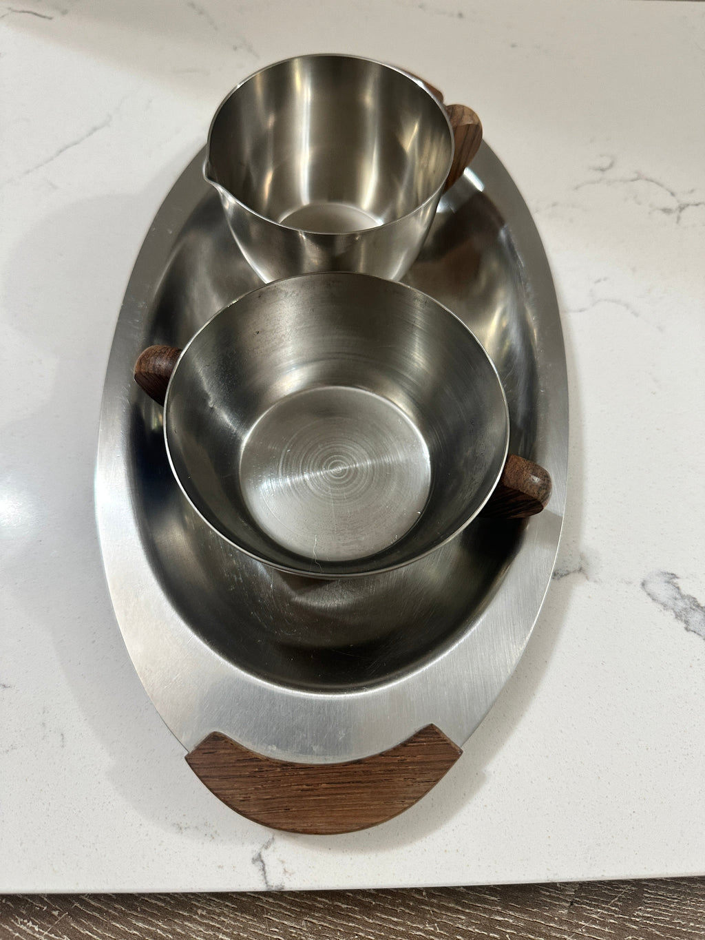 The Collected Chapter vintage Danish Modern stainless steel creamer and sugar set with wood handles on an oval tray.