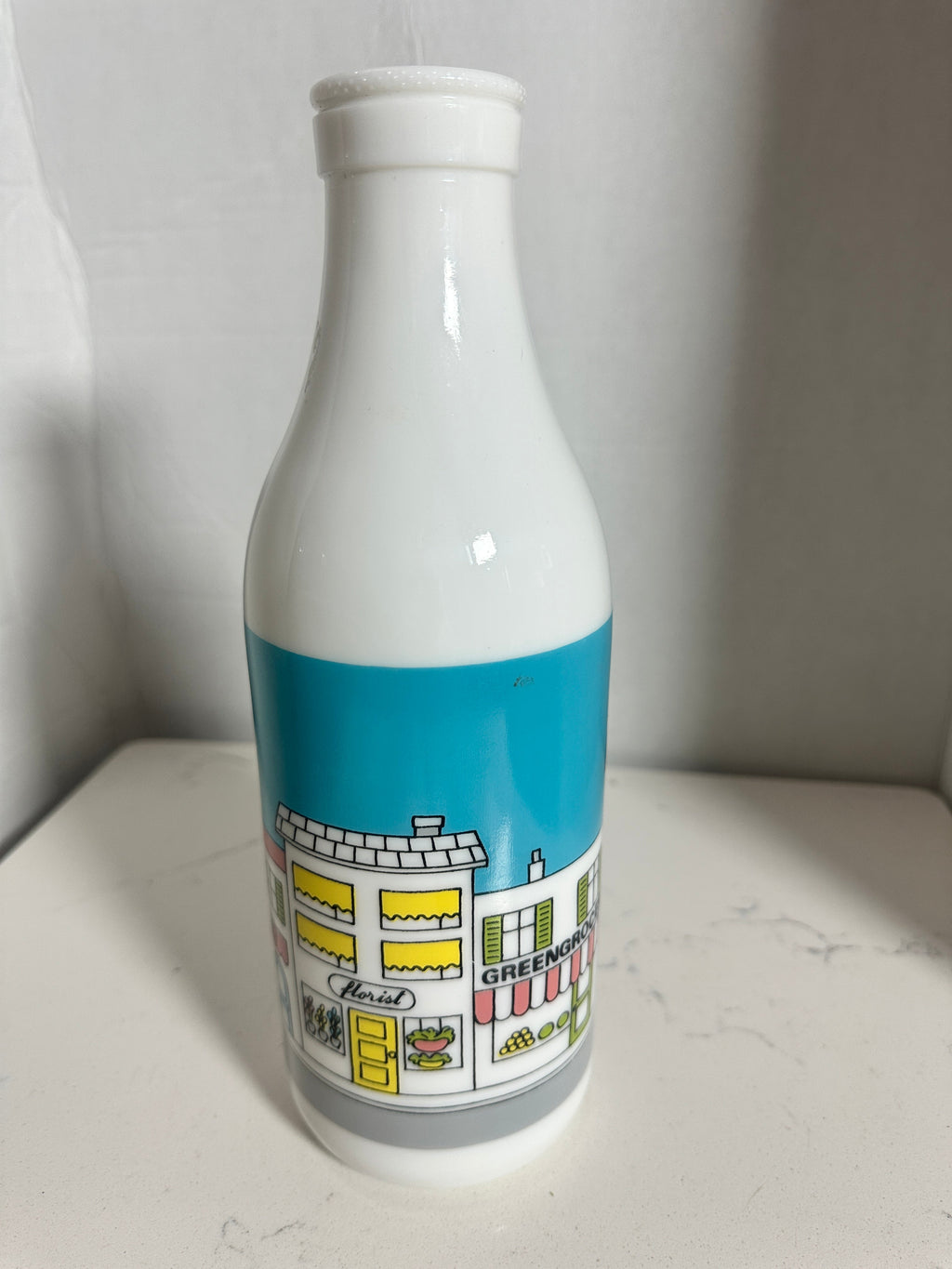 The Collected Chapter vintage white milk glass bottle vase featuring a colorful illustrated street scene graphic.