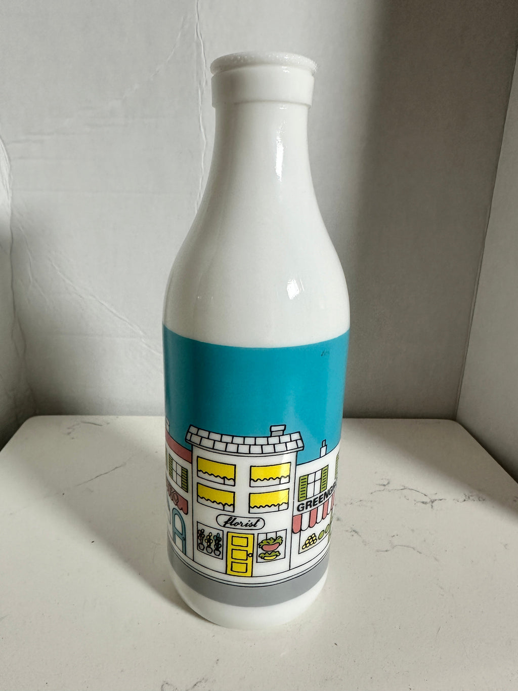 The Collected Chapter vintage white milk glass bottle vase featuring a colorful illustrated street scene graphic.