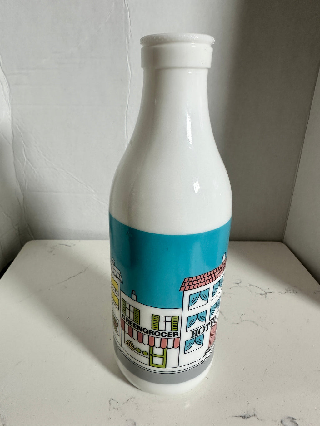 The Collected Chapter vintage white milk glass bottle vase featuring a colorful illustrated street scene graphic.