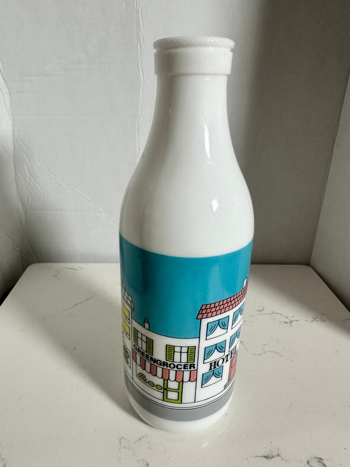 The Collected Chapter vintage white milk glass bottle vase featuring a colorful illustrated street scene graphic.