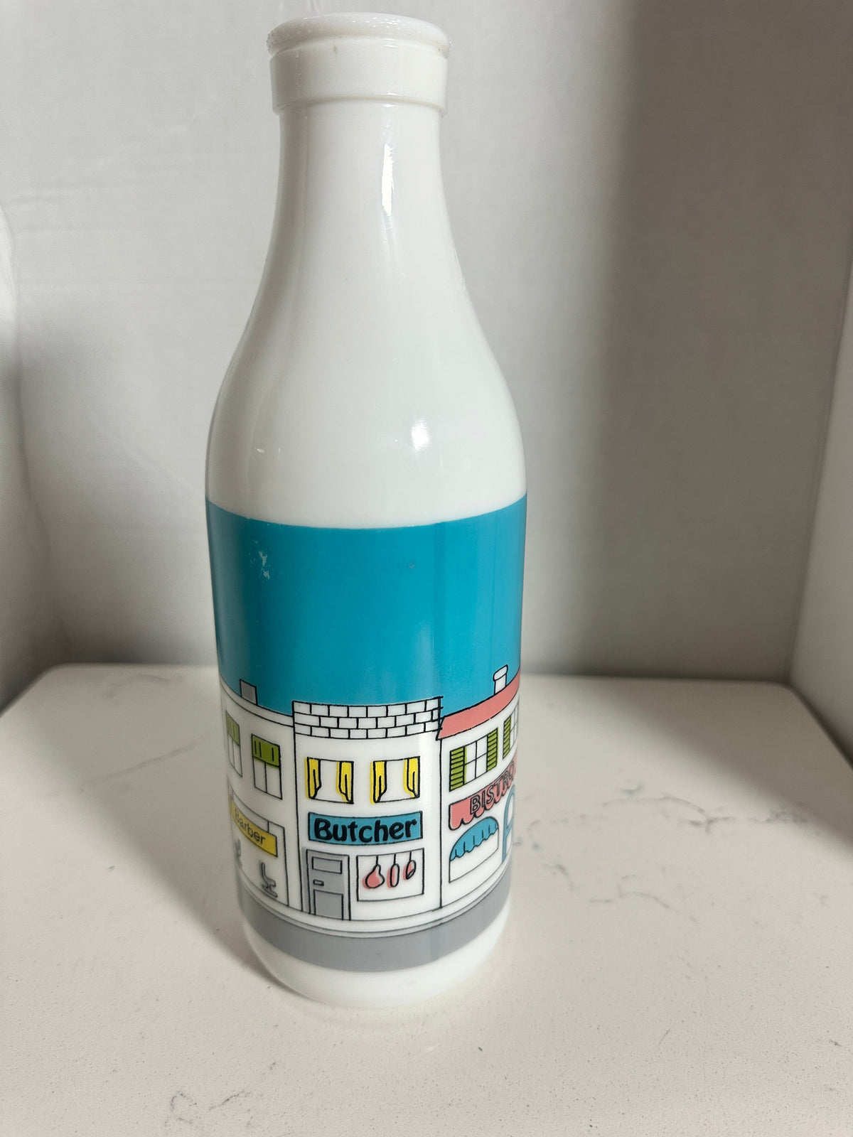 The Collected Chapter vintage white milk glass bottle vase featuring a colorful illustrated street scene with shops.