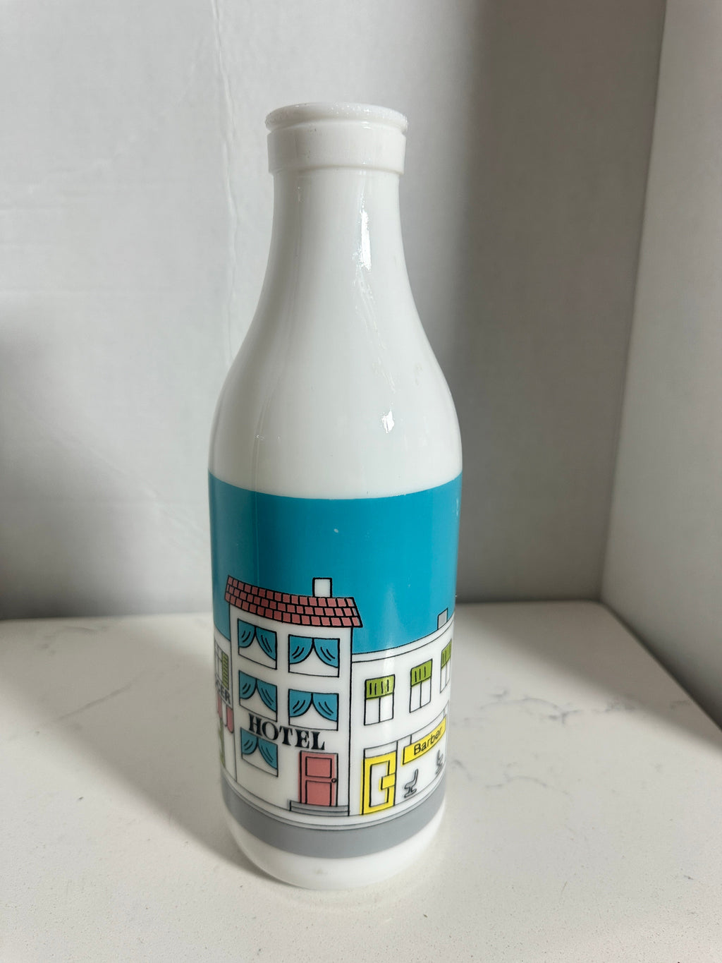 The Collected Chapter vintage white milk glass bottle vase featuring a colorful illustrated street scene graphic.