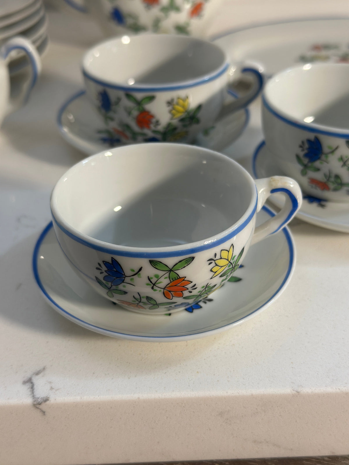 The Collected Chapter vintage miniature porcelain tea cup and saucer with a colorful floral pattern and blue trim.