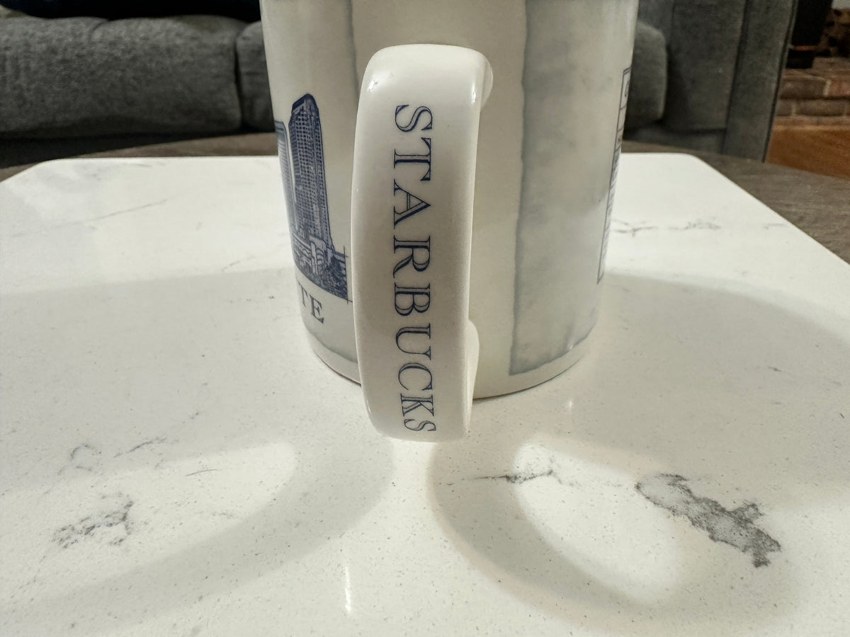 The Collected Chapter 2007 Starbucks Charlotte Queen City mug handle with vertical branding on a white marble surface