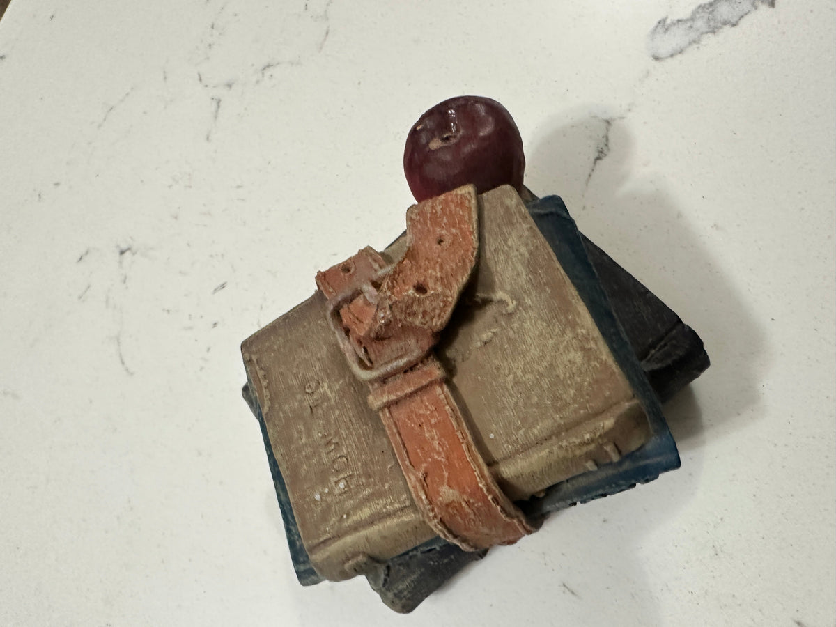 The Collected Chapter vintage-style figurine of three stacked books with a buckled strap and a red apple on top.