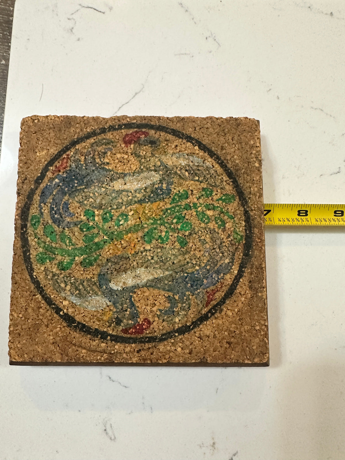 The Collected Chapter vintage square cork trivet with a stylized peacock bird design, green foliage, and red accents.