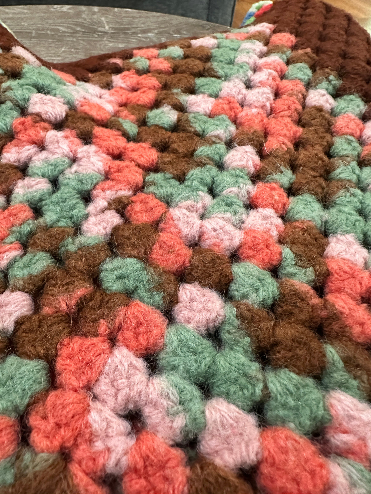The Collected Chapter vintage handmade crochet granny square afghan with textured brown, pink, and sage green yarn.