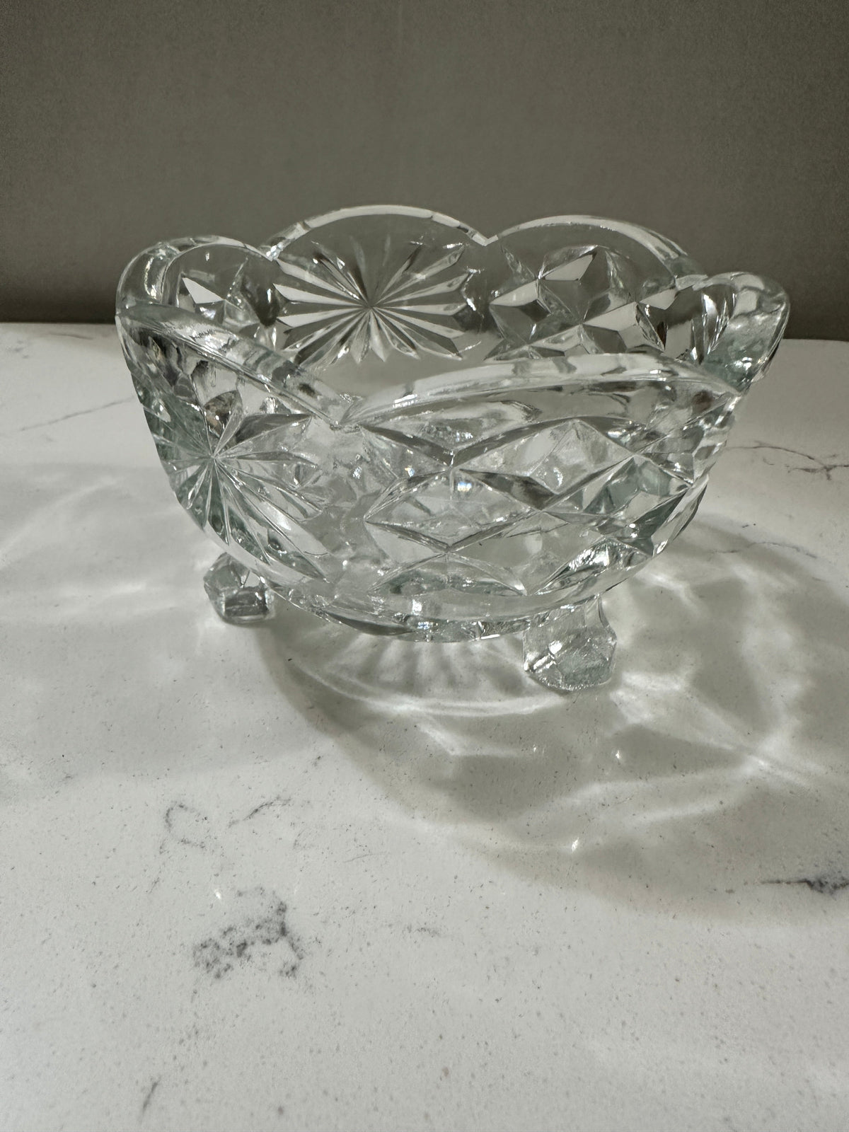 The Collected Chapter vintage clear crystal bowl with three feet, scalloped rim, and starburst geometric patterns.