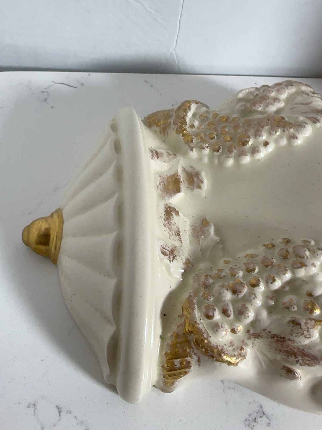 The Collected Chapter vintage resin wall-mounted grape dispenser in cream with ornate gold grape and vine detailing.