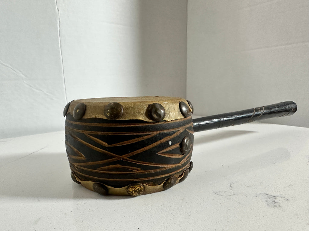 The Collected Chapter vintage handcrafted drum with natural hide head, carved wooden handle, and metal stud accents.