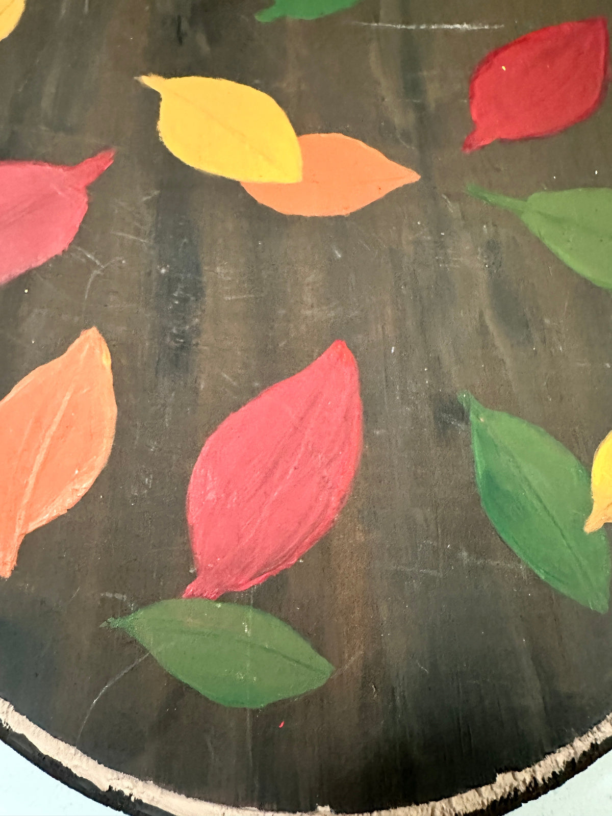 The Collected Chapter vintage hand-painted oval wooden plaque featuring colorful autumn leaves on a black background.