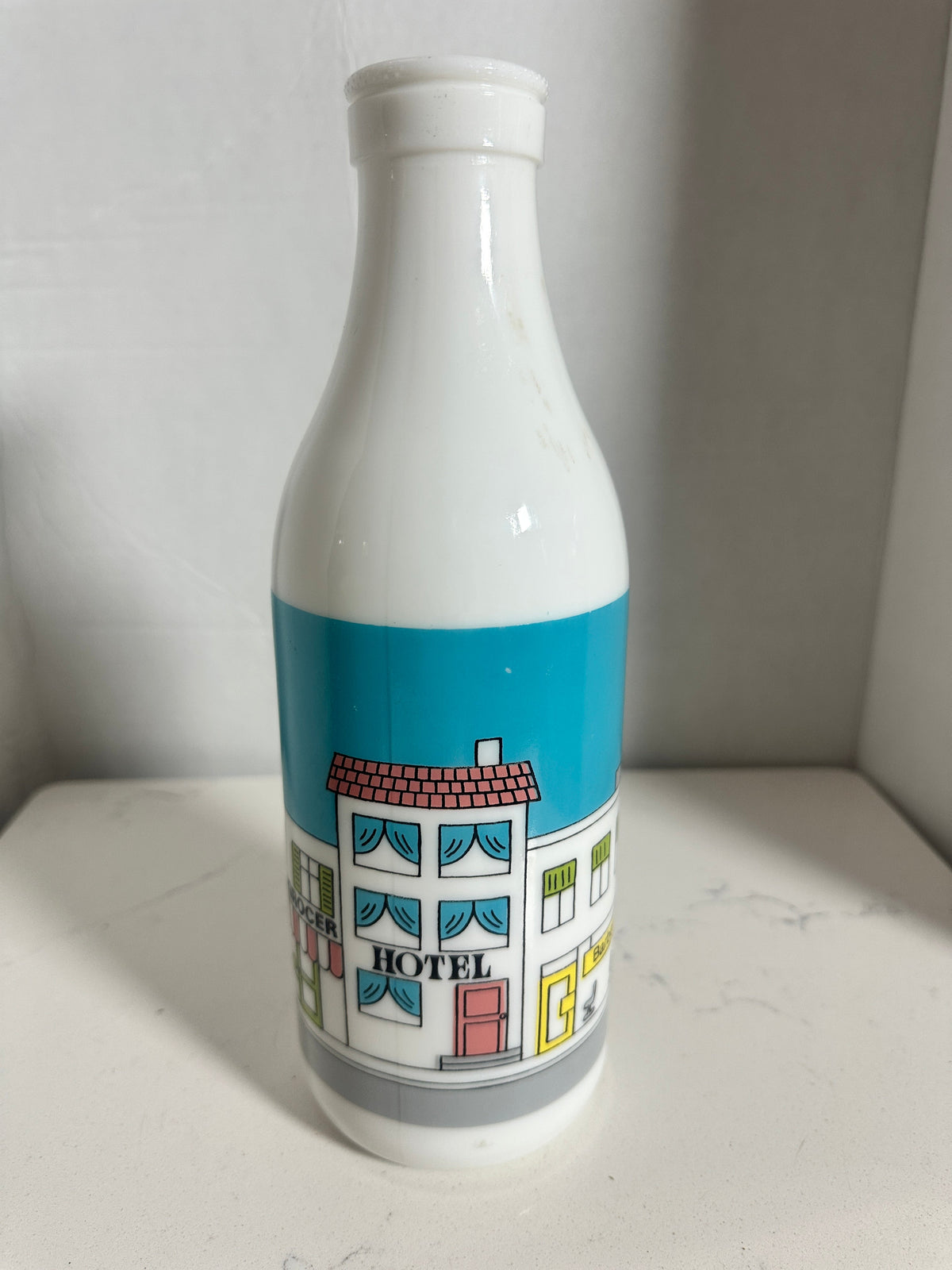 The Collected Chapter vintage white milk glass bottle vase featuring a colorful illustrated street scene graphic.