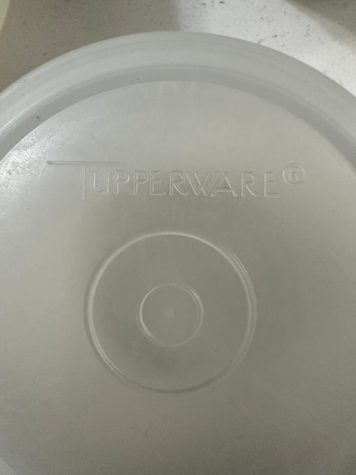 The Collected Chapter vintage Tupperware lid with embossed logo detail on a translucent plastic surface